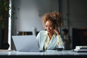 Woman working on laptop at desk, looking thoughtful.